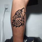 Tribal wolf tattoo on a man's arm, showcasing intricate black ink design.