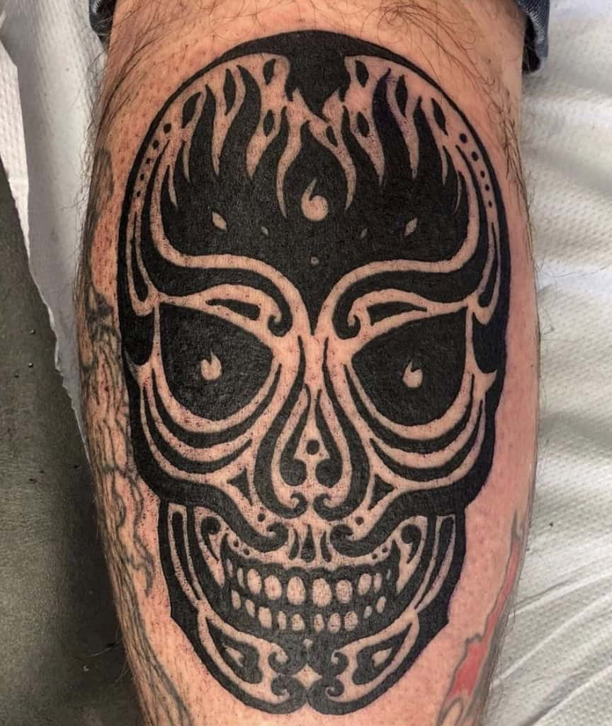 Tribal skull tattoo on a man's arm, featuring a skull design with bold tribal patterns and shading.