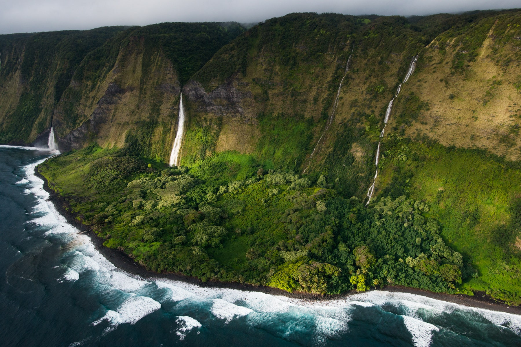 Lush waterfalls cascade down cliffs between Waipio and Waimanu Valleys on the Big Island, Hawaii