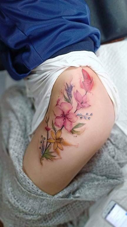 Colorful floral tattoo on upper thigh featuring pink, yellow, and purple flowers with green leaves, artistically detailed.