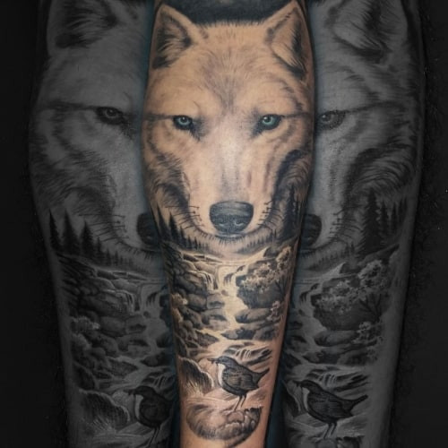 A white wolf tattoo on a man's arm, rendered in white and grey ink to capture the arctic wolf's distinctive fur and symbolism of purity, resilience, and good fortune.