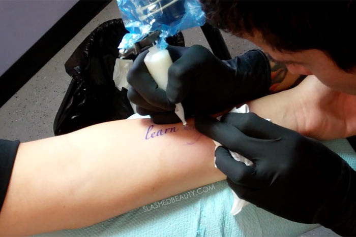 White ink being tattooed over a stencil, highlighting the technique required.