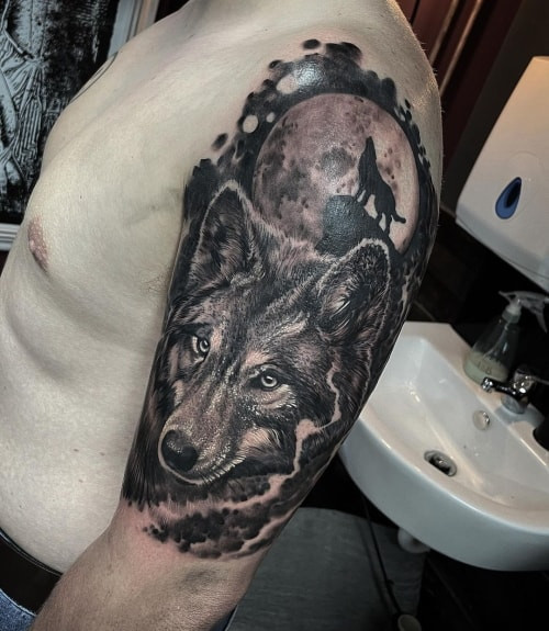 A dramatic wolf and moon tattoo on a man's thigh, featuring a wolf silhouetted against a detailed moon, symbolizing mystery, transformation, and primal instincts.