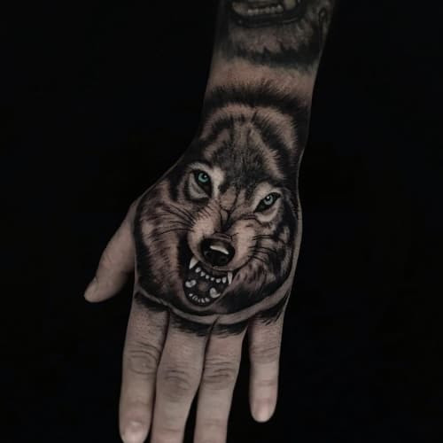 A realistic wolf head tattoo on a man's hand, focusing on the wolf's intense gaze and detailed fur texture to convey focused power and direct expression.