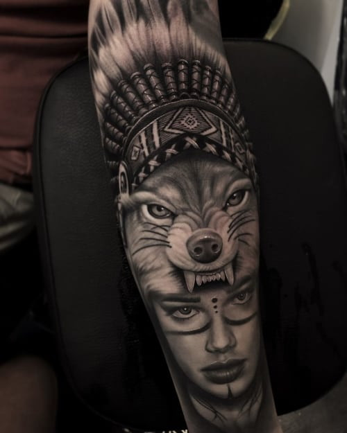 A wolf headdress tattoo on a man's back, featuring a woman wearing a wolf headdress, symbolizing strength, protection, and the embodiment of wolf-like qualities.