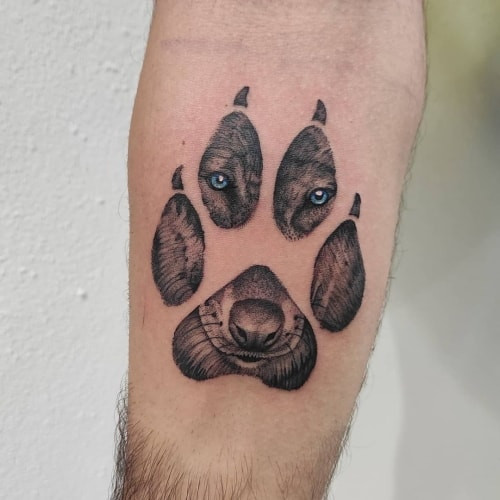 A wolf paw tattoo on a man's calf, featuring detailed paw prints in black ink, symbolizing determination, progress, and following a unique life path.