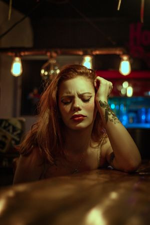 Woman Feeling Sick Sitting at Bar with Tattoo on her forearm