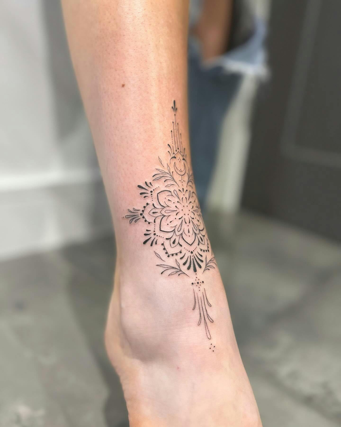 Ornamental ankle tattoo, intricate decorative design on ankle.