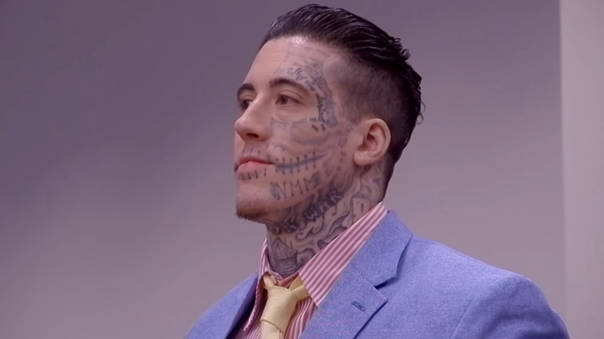 Wade Wilson at jury selection in 2024, wearing a suit but with extensive facial and neck tattoos visible, including a skull shadow and &quot;HA HA HA&quot; near his eye.