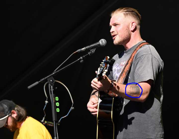 Zach Bryan performing, showcasing his book tattoo.