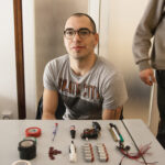 Tools for homemade tattoo machine including scissors, pliers, batteries, toothbrush, lighter, tape, motor, glue, knife, and screwdrivers
