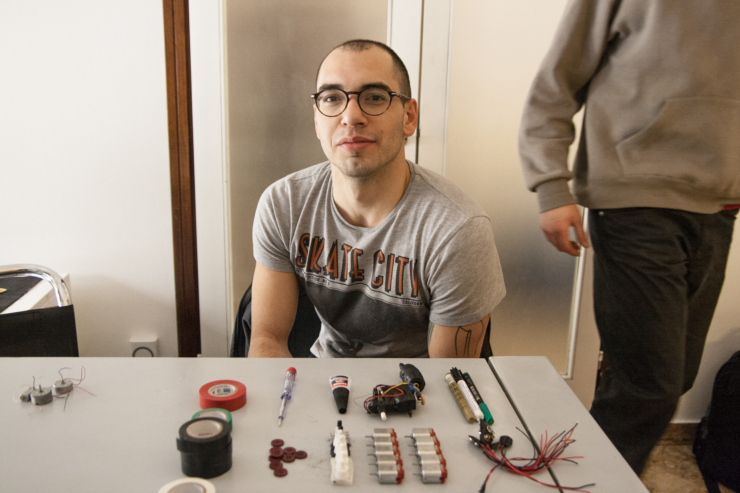 Tools for homemade tattoo machine including scissors, pliers, batteries, toothbrush, lighter, tape, motor, glue, knife, and screwdrivers