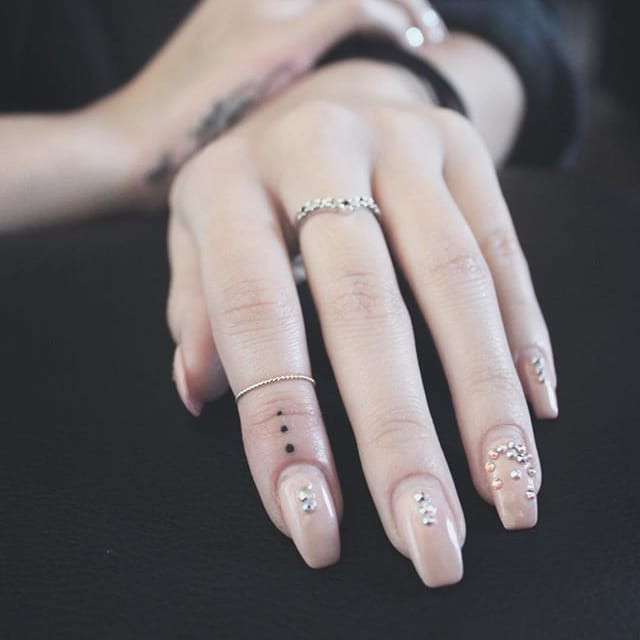 A close-up shot of a hand featuring a three-dot tattoo on the finger.