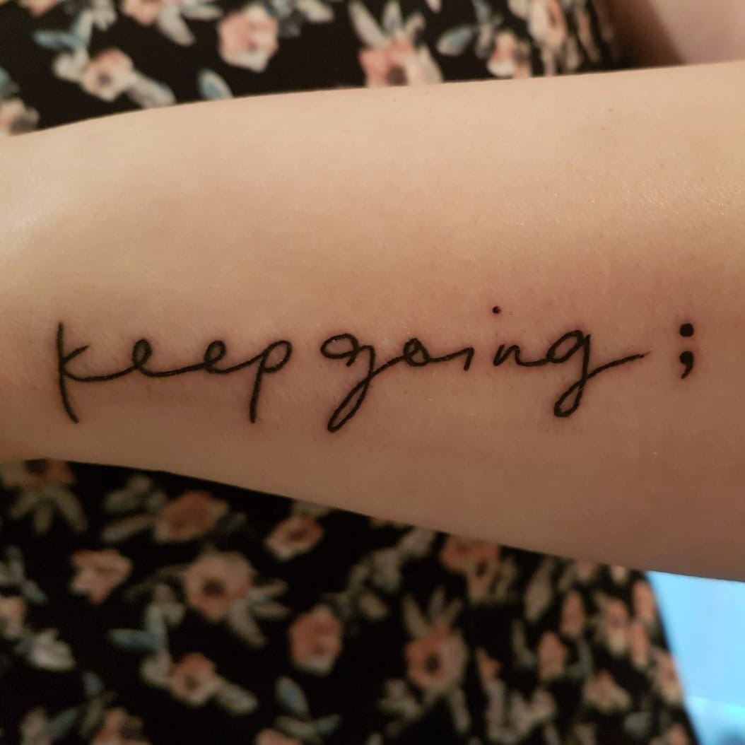 A close-up of a finger tattoo featuring a semicolon.