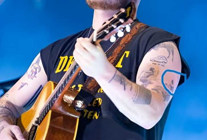 Zach Bryan performing at the Railbird Music Festival, displaying his phoenix tattoo.