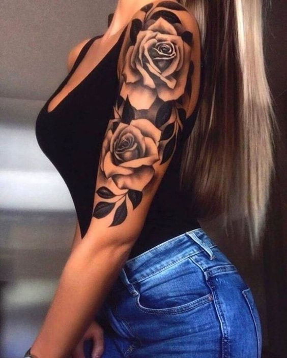 Rose vine with thorns tattoo on arm of woman wearing a black top, showcasing floral design.