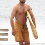 Joshua Jackson showing off his tribal armband tattoo while surfing in Montauk, New York, highlighting his toned physique and casual style