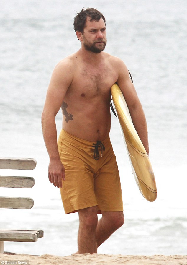 Joshua Jackson showing off his tribal armband tattoo while surfing in Montauk, New York, highlighting his toned physique and casual style