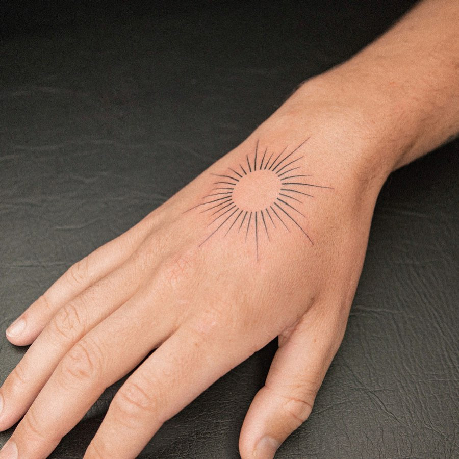 A sun tattoo design on a woman's hand, featuring straight lines as rays that create an illusion of a circle.