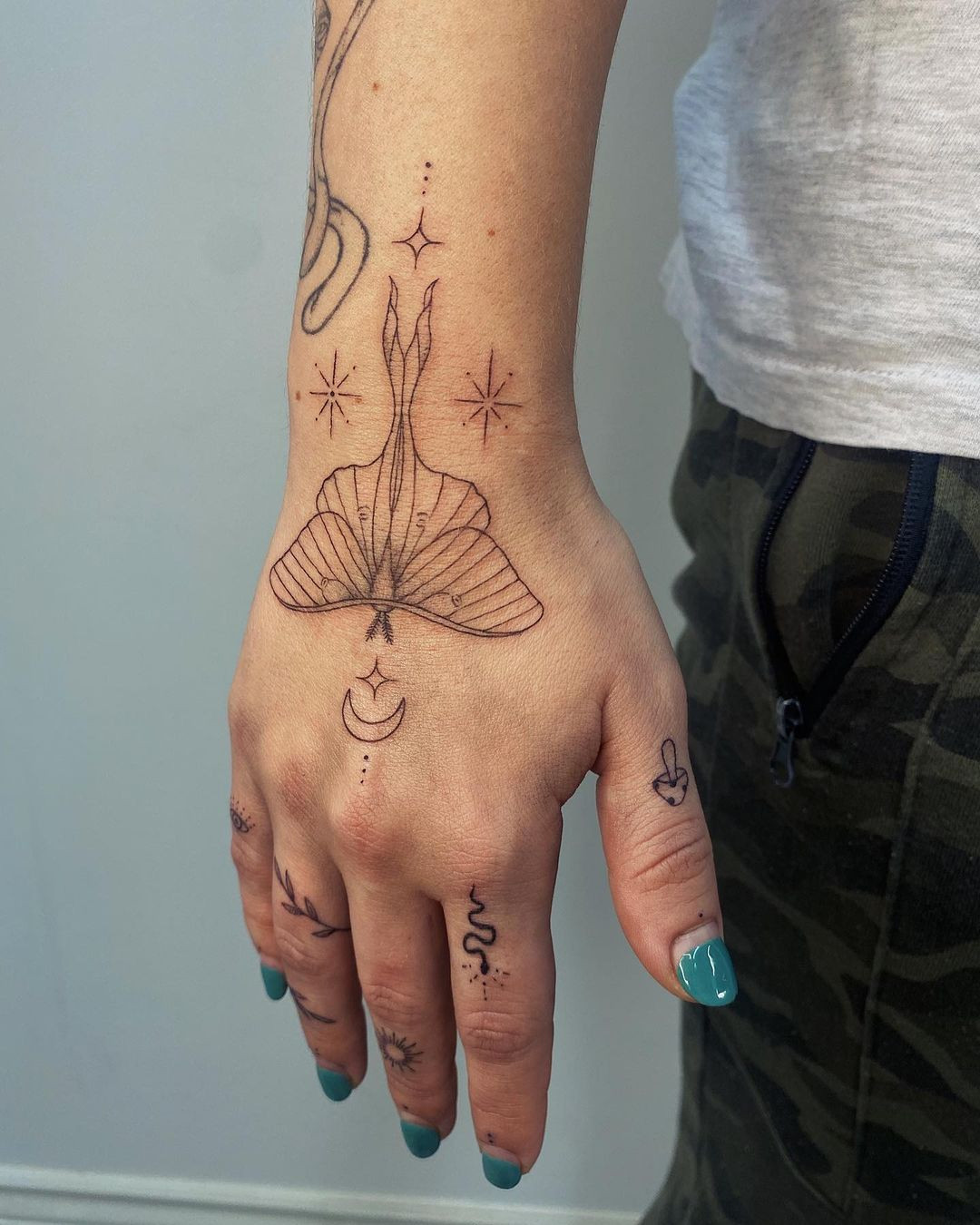 A luna moth tattoo on a woman's hand, representing metamorphosis, quest for knowledge, and self-acceptance.