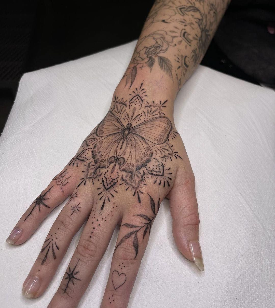 A butterfly mandala tattoo on a woman's hand, featuring a butterfly with a mandala effect and intricate details.