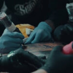 Tattoo artist tattooing client under surgical gloves.