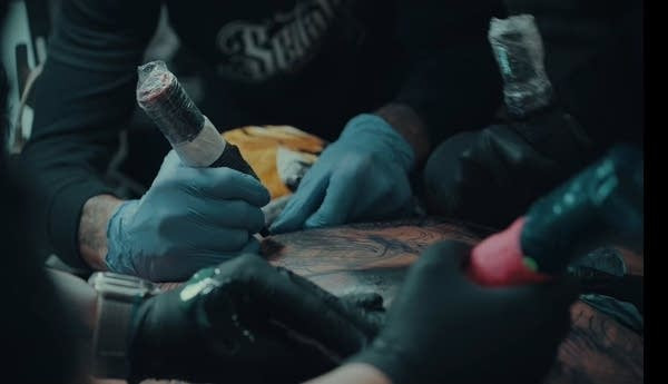 Tattoo artist tattooing client under surgical gloves.