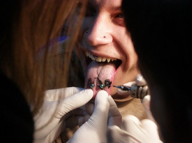 Various minimalist tongue tattoo designs including a small cross, music note, and dot
