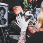 A tattoo artist making a tattoo and copying a design from a tablet.
