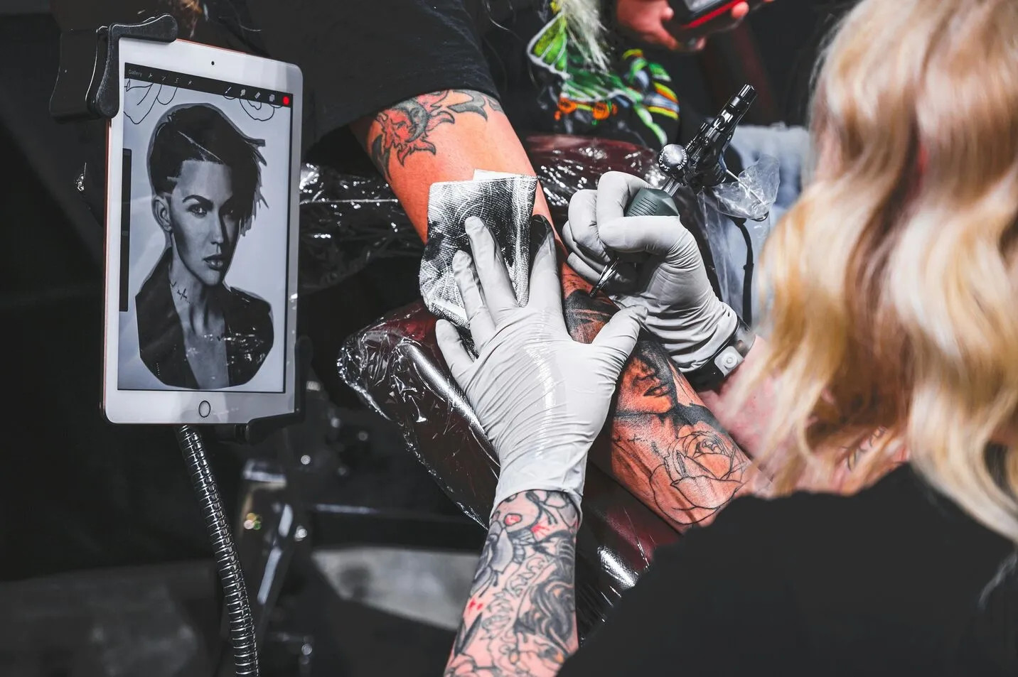 A tattoo artist making a tattoo and copying a design from a tablet.