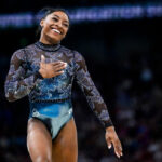 simone biles smiles and holds up her right hand