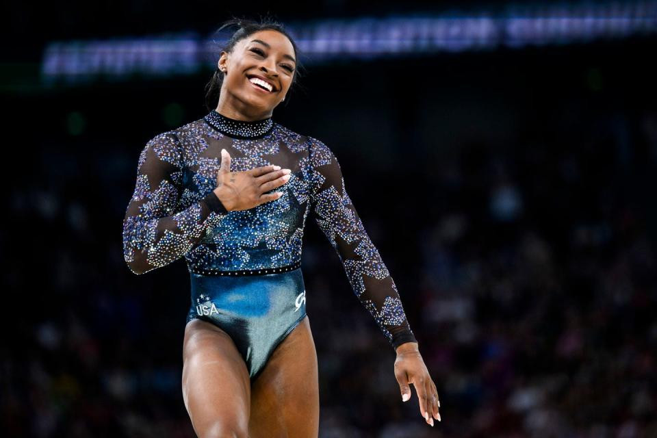 simone biles smiles and holds up her right hand