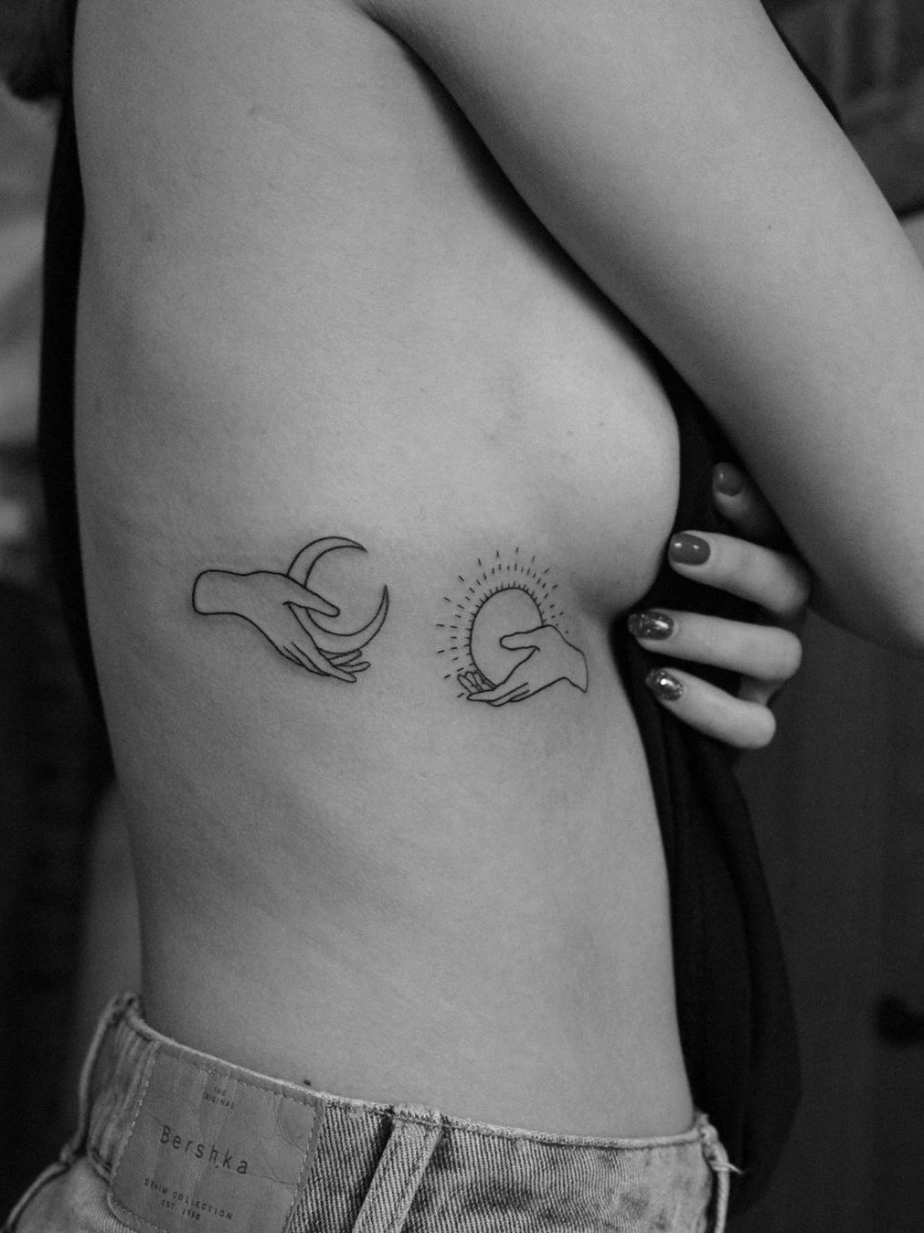 A pair of fingers adorned with sun and moon tattoos.