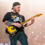 Zach Bryan performing onstage, showcasing his bronco tattoo.