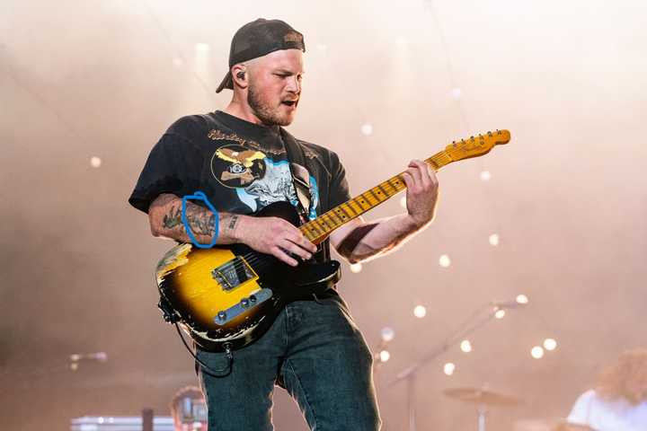 Zach Bryan performing onstage, showcasing his bronco tattoo.