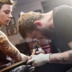 A tattoo artist working on a detailed spine tattoo