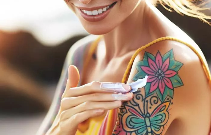 A woman applying sunscreen to her shoulder tattoo