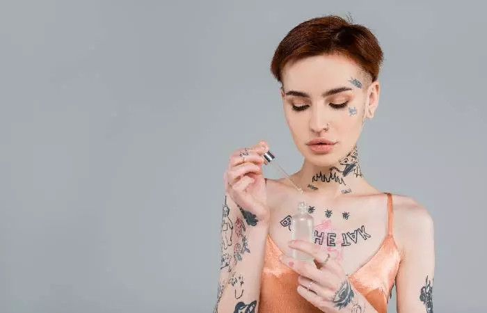 A woman with tattoos holding a bottle of serum for application