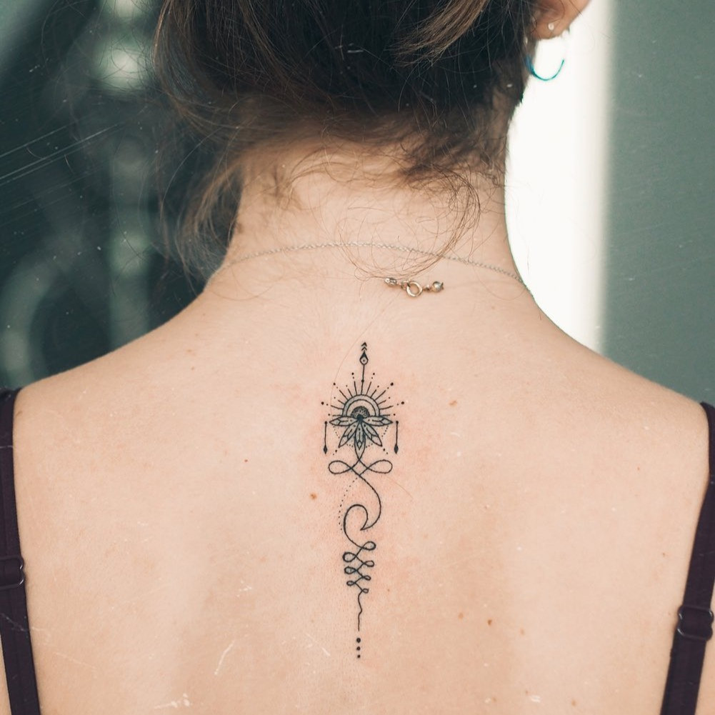 A finger adorned with a minimalist Unalome tattoo design.