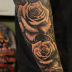 Black rose sleeve tattoo on arm, featuring intricate details and shading.