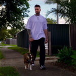A man with tattoos walks his dog in a suburban street
