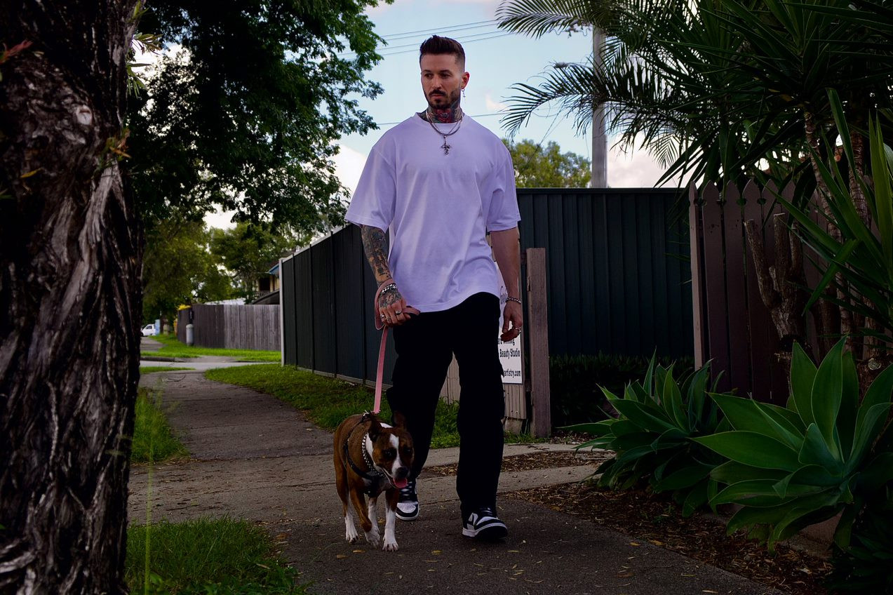 A man with tattoos walks his dog in a suburban street