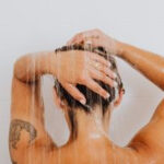 Woman gently washing her tattooed arm in the shower, demonstrating proper tattoo aftercare.