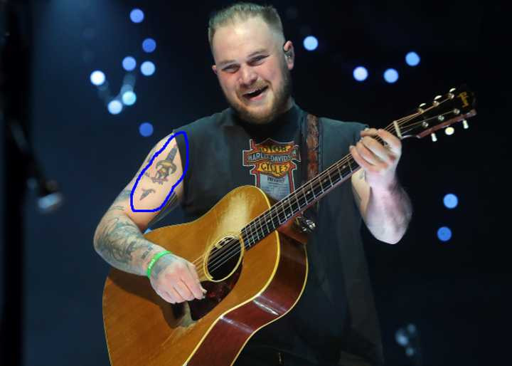 Zach Bryan performing, displaying his broken sword tattoo.