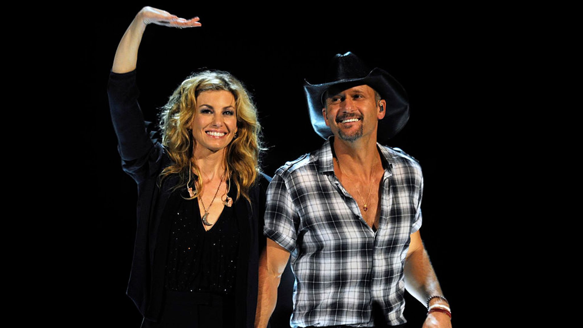 Faith Hill and Tim McGraw holding hands as they walk on stage. Faith waves at the crowd with her other hand.