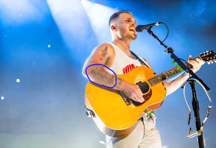 Zach Bryan performing at Summerfest, displaying his cowboy on a bronco tattoo.