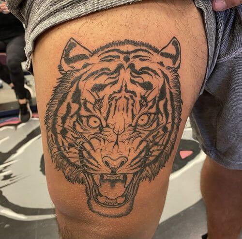 Lion tattoo on a man's thigh symbolizes courage and strength with sharp fangs displayed