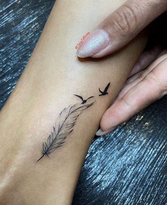 Minimalistic feather and birds tattoo on wrist, detailed feather design with two flying birds, delicate and elegant ink art.
