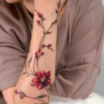 Elegant floral upper arm tattoo featuring delicate blossoms and green leaves