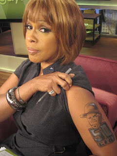 Gayle King playfully displaying a temporary 50 Cent tattoo, showcasing her sense of humor during an interview and demonstrating her engagement with popular culture
